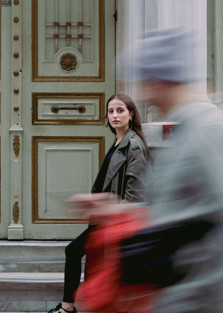 Femme immobile sur un seuil de porte pendant que des passants flous défilent : métaphore de la scansion, cette pause nécessaire pour préserver le rythme de travail